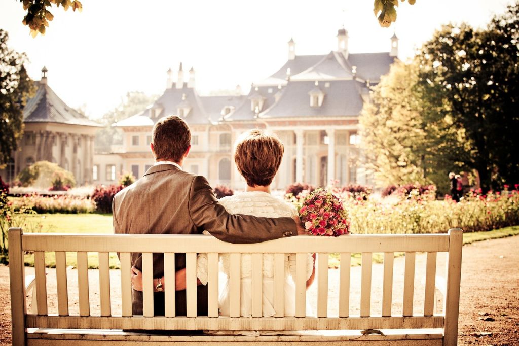 Un couple assis sur un banc avec un bouquet de rose devant un jardin